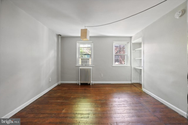 empty room featuring dark hardwood / wood-style floors, radiator, and built in shelves