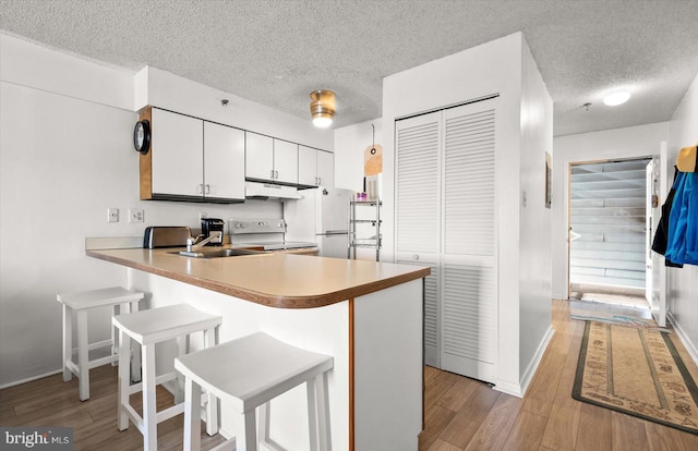 kitchen with kitchen peninsula, white cabinets, a textured ceiling, light hardwood / wood-style floors, and white appliances