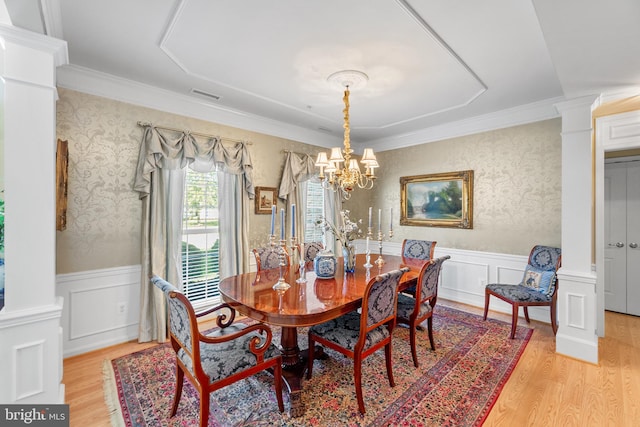 dining space with an inviting chandelier, light wood-type flooring, crown molding, and ornate columns