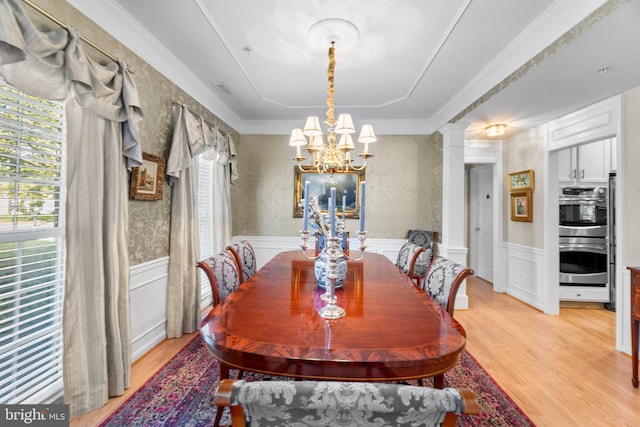 dining area featuring a notable chandelier, light hardwood / wood-style floors, crown molding, and decorative columns