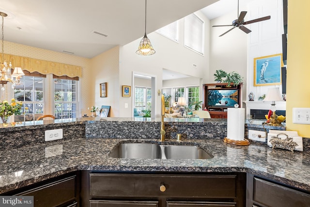 kitchen featuring dark brown cabinets, hanging light fixtures, dark stone countertops, and ceiling fan