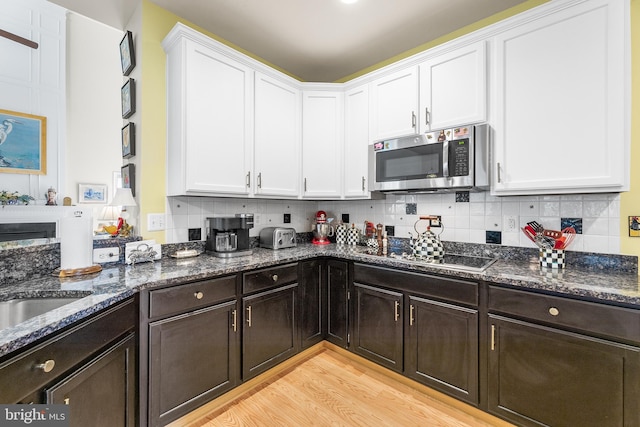 kitchen with electric cooktop, dark stone counters, light wood-type flooring, and white cabinetry