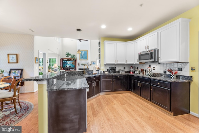 kitchen with kitchen peninsula, light hardwood / wood-style floors, dark stone counters, and white cabinetry