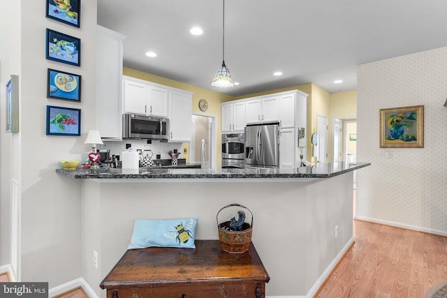 kitchen with stainless steel appliances, hanging light fixtures, kitchen peninsula, and white cabinetry