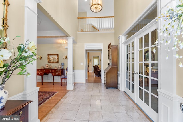 foyer entrance featuring french doors, decorative columns, a high ceiling, crown molding, and light hardwood / wood-style floors