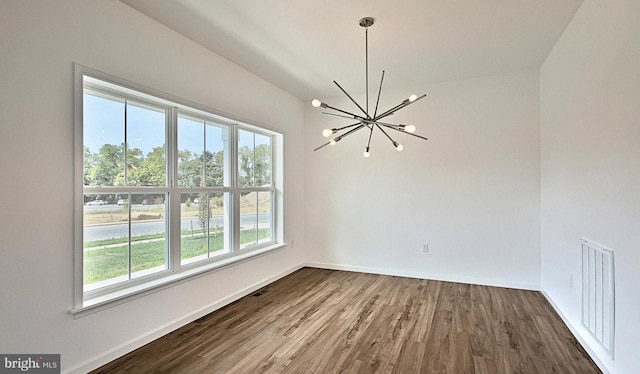 spare room with wood-type flooring, an inviting chandelier, and a healthy amount of sunlight