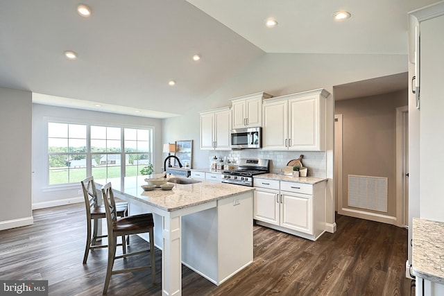 kitchen with white cabinets, an island with sink, appliances with stainless steel finishes, light stone countertops, and sink