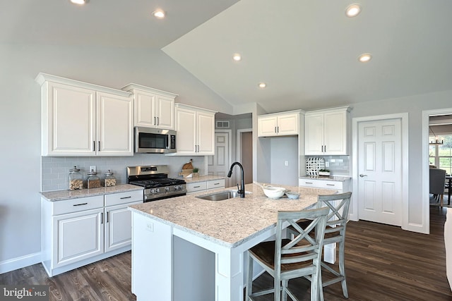 kitchen featuring white cabinets, a center island with sink, appliances with stainless steel finishes, vaulted ceiling, and sink