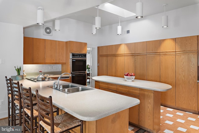 kitchen featuring a breakfast bar area, kitchen peninsula, sink, decorative light fixtures, and black double oven