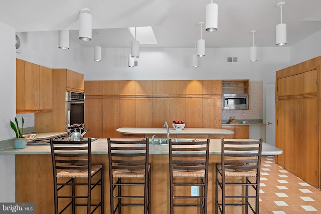 kitchen with a skylight, a kitchen bar, hanging light fixtures, stainless steel appliances, and decorative backsplash