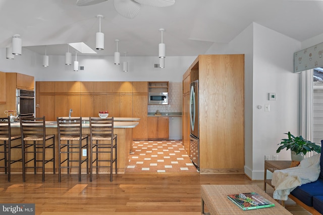 kitchen with a skylight, a kitchen bar, light hardwood / wood-style floors, stainless steel appliances, and decorative light fixtures