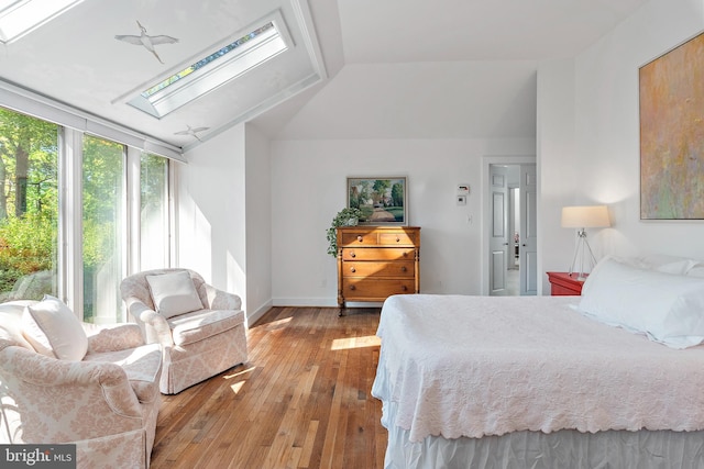 bedroom featuring lofted ceiling with skylight and light hardwood / wood-style floors