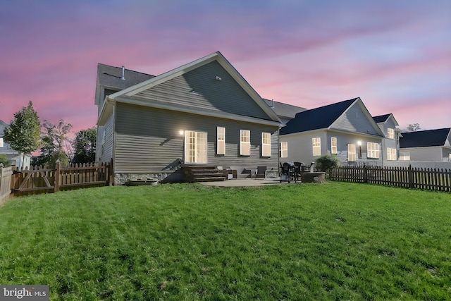 back house at dusk featuring a patio area and a lawn