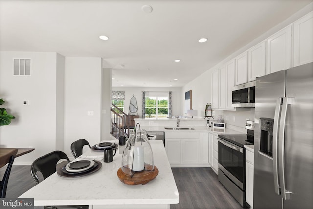 kitchen featuring white cabinets, sink, appliances with stainless steel finishes, dark hardwood / wood-style floors, and a breakfast bar