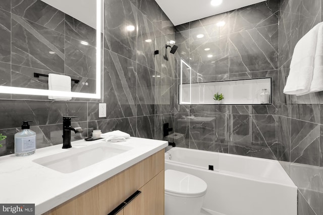 full bathroom with tiled shower / bath, vanity, tile walls, and toilet