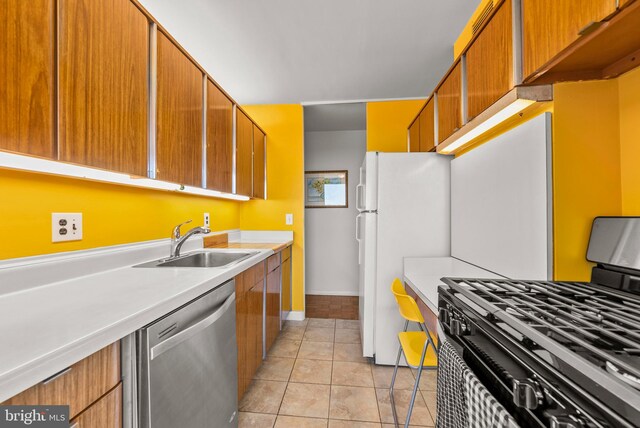 kitchen featuring stainless steel dishwasher, gas range, light tile patterned flooring, white fridge, and sink