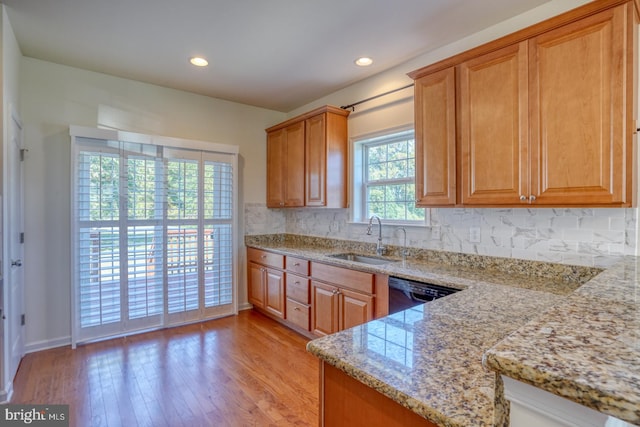 kitchen featuring light wood-type flooring, light stone countertops, decorative backsplash, sink, and dishwasher