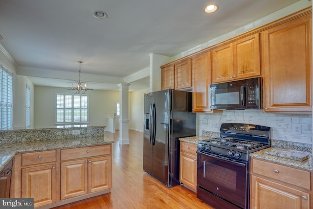 kitchen featuring light hardwood / wood-style flooring, a notable chandelier, decorative columns, light stone countertops, and black appliances