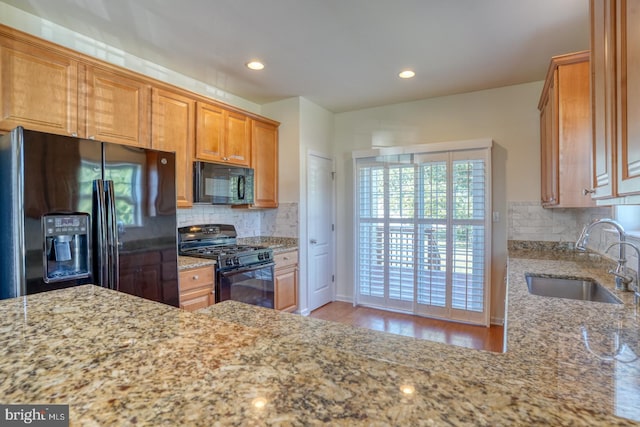 kitchen with light stone counters, sink, light hardwood / wood-style flooring, backsplash, and black appliances