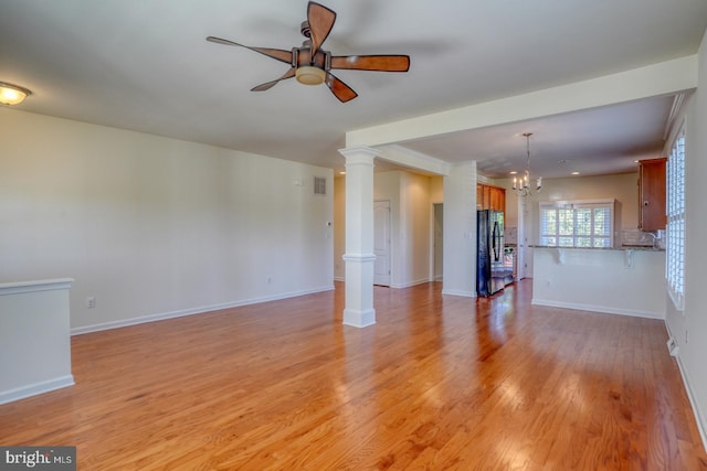 unfurnished living room with ceiling fan with notable chandelier, decorative columns, and light wood-type flooring