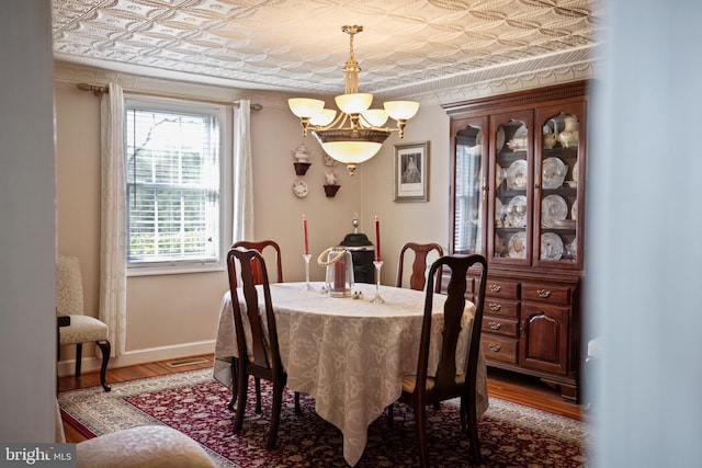 dining space featuring wood finished floors, an inviting chandelier, baseboards, and an ornate ceiling