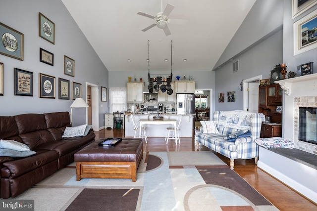 living area with visible vents, ceiling fan, wood finished floors, high vaulted ceiling, and a premium fireplace