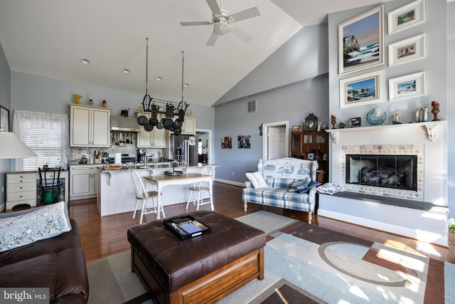 living room featuring ceiling fan, high vaulted ceiling, dark wood-type flooring, visible vents, and a tile fireplace