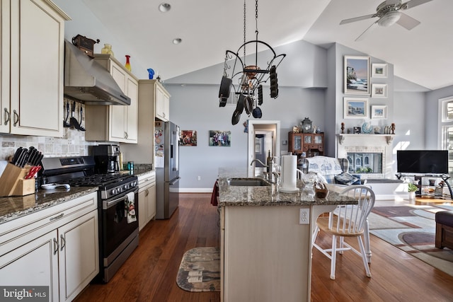 kitchen with a sink, wall chimney range hood, open floor plan, a center island with sink, and stainless steel appliances
