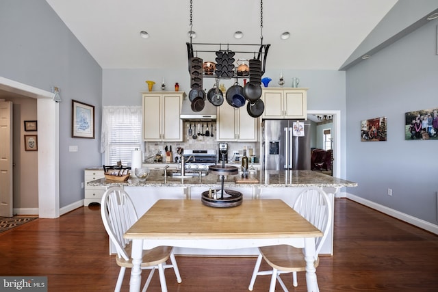 kitchen with cream cabinets, light stone counters, dark wood-type flooring, and stainless steel appliances