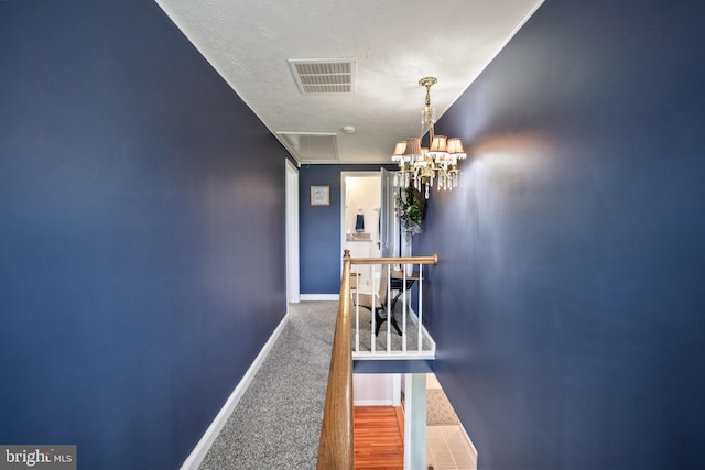corridor with an inviting chandelier, visible vents, carpet floors, attic access, and baseboards