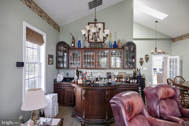 bar with decorative light fixtures, vaulted ceiling, a chandelier, and dark brown cabinets