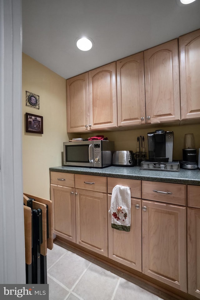 kitchen with light brown cabinets, stainless steel microwave, and dark countertops