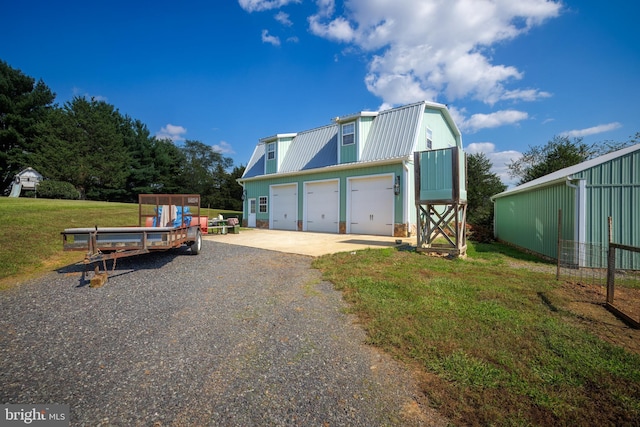 view of property exterior with metal roof, a lawn, an outbuilding, a gambrel roof, and driveway