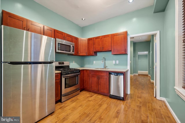 kitchen with appliances with stainless steel finishes, sink, and light hardwood / wood-style flooring