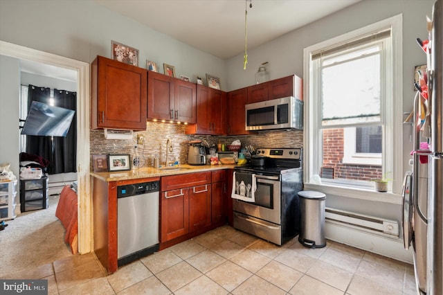 kitchen featuring light tile patterned floors, sink, baseboard heating, stainless steel appliances, and decorative backsplash