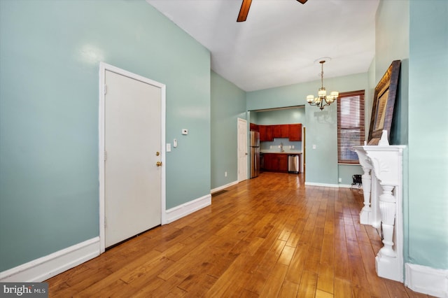 unfurnished living room with ceiling fan with notable chandelier and hardwood / wood-style flooring