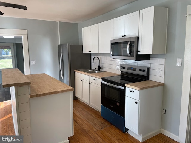 kitchen with appliances with stainless steel finishes, white cabinetry, butcher block counters, and sink