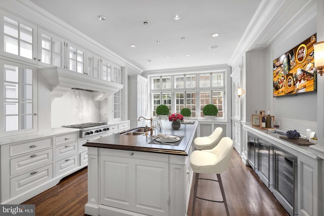 kitchen featuring dark hardwood / wood-style floors, white cabinetry, crown molding, and a center island with sink