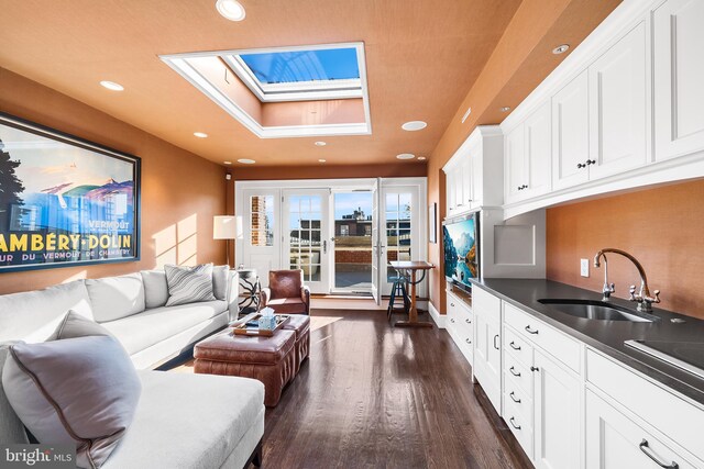 living room featuring dark hardwood / wood-style floors, a raised ceiling, sink, and a skylight