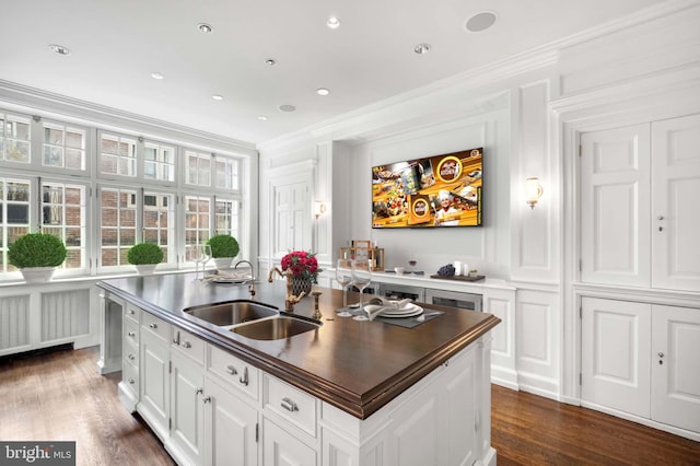 kitchen featuring radiator, sink, crown molding, a center island with sink, and white cabinets