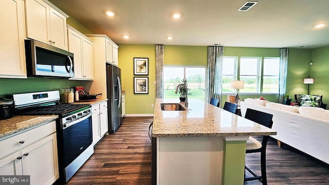 kitchen with dark hardwood / wood-style floors, white cabinetry, appliances with stainless steel finishes, a center island with sink, and a kitchen breakfast bar