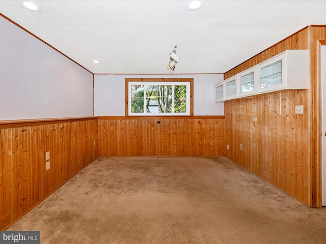 carpeted empty room with a textured ceiling, wood walls, and crown molding