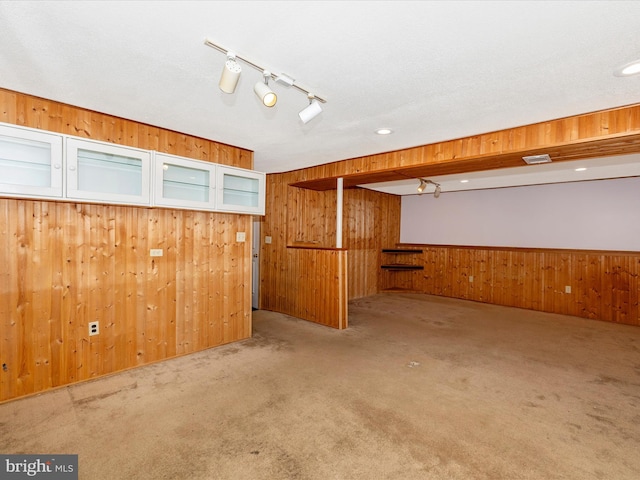 basement featuring rail lighting, wooden walls, and light carpet