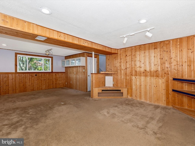 interior space with a textured ceiling, wood walls, rail lighting, and carpet flooring