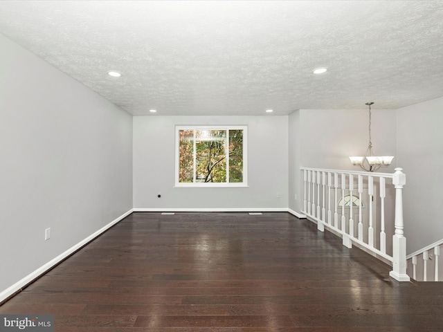 empty room with dark hardwood / wood-style floors, an inviting chandelier, and a textured ceiling