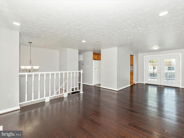 empty room featuring french doors, a chandelier, dark hardwood / wood-style floors, and a textured ceiling