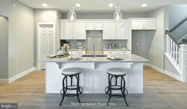 kitchen featuring light stone counters, a center island with sink, white cabinetry, and sink