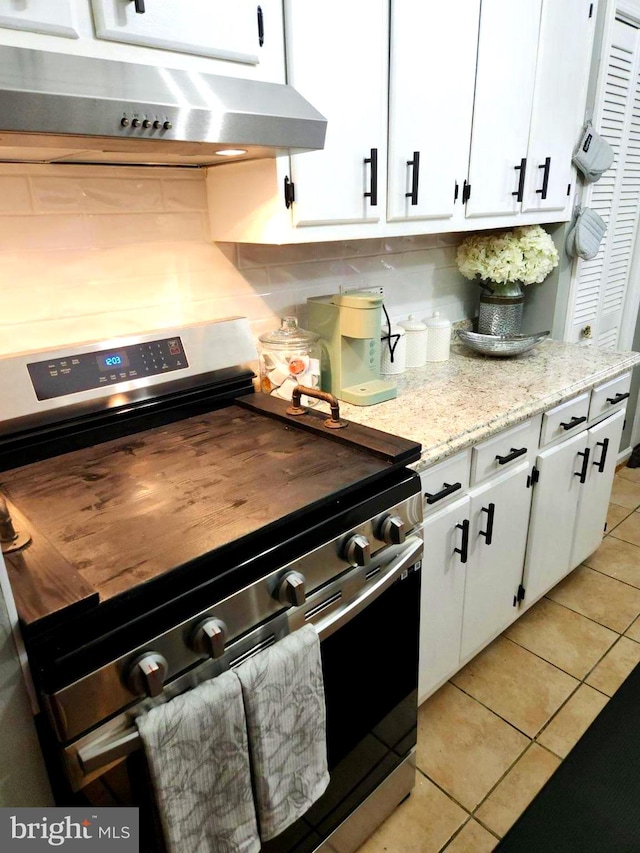 kitchen featuring backsplash, stainless steel stove, light tile patterned floors, light stone countertops, and white cabinets