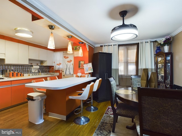 kitchen with ornamental molding, a breakfast bar area, hardwood / wood-style floors, and white cabinets