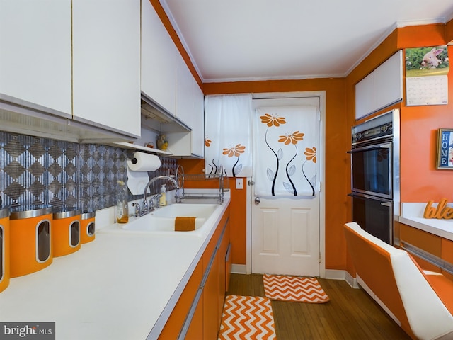 kitchen featuring decorative backsplash, white cabinets, double oven, dark wood-type flooring, and sink